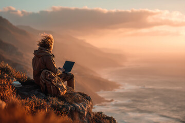Person using a laptop on a cliffside at sunset with ocean views