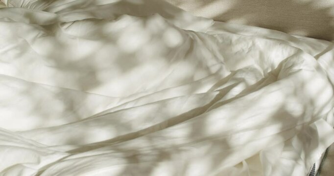 Sunlight streams through a window, casting dancing shadows of leaves on an unmade bed. The soft, white linens invite relaxation and rest. Perfect for lifestyle, home decor, or sleep-related projects.