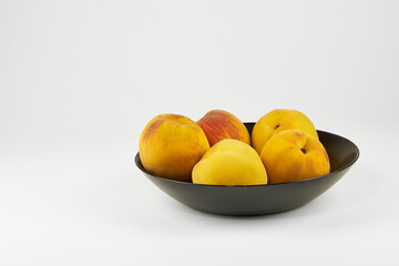 Peaches isolated on a black plate in close-up, arranged on a light background with copy space