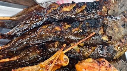 Grilled fish on skewers with crispy skin served on metal tray in outdoor culinary setting