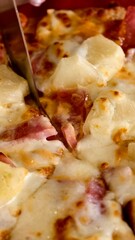 Deliciously cheesy ham and pineapple pizza being sliced with a sharp knife in a close-up view