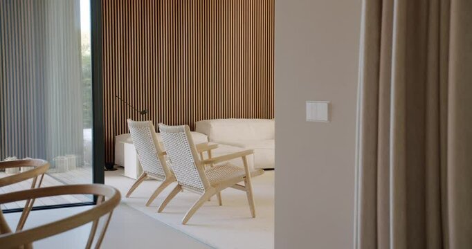 A calico cat walks through a modern, minimalist home with light wood and neutral colors. The cat explores the space, adding a touch of life to the serene setting.