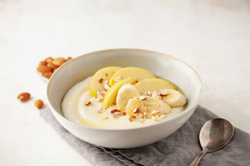 Sweet milky semolina porridge with apples bananas and almonds in a bowl on the table. Healthy children's breakfast.