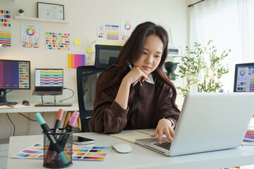 Graphic designer using laptop while working on new project at a creative desk.