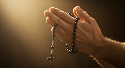 Close up of praying hands holding a rosary with a cross in a dimly lit and warm light setting