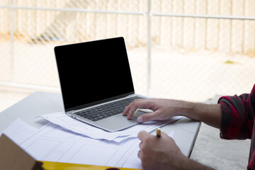 Male architect working with laptop on blueprint architects project in outdoor office.