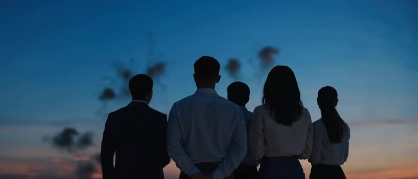 Five office colleagues stand in silhouette admiring bright fireworks against twilight sky. Concept of corporate achievement and shared celebration