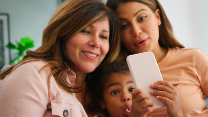 Multi-Generation Female Hispanic Family At Home Pulling Funny Faces For Selfie On Mobile Phone
