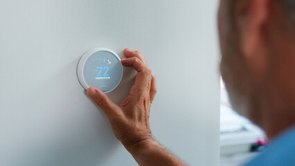 Senior Hispanic Man Adjusting Digital Central Heating Thermostat In Home