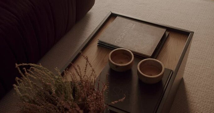 A cozy living room setup featuring a stylish coffee table with books, wooden bowls, and decorative plants. Warm, inviting atmosphere, perfect for relaxing moments. Modern home decor inspiration.