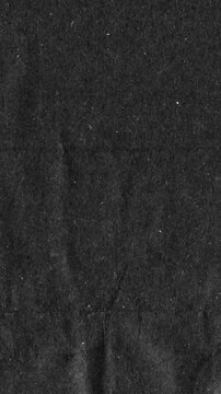 Black kraft paper noise texture vertical stop motion video. Old page overlay effect background loop animation. Vintage paper texture with crease, stain, grain, dust particles. Empty animated backdrop