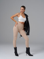 Elegant woman poses confidently in a sleek outfit. She wears a white crop top, beige leggings,...