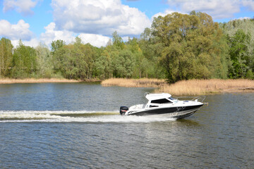 Obraz premium Motorboat on the Water with trees and clouds on the background