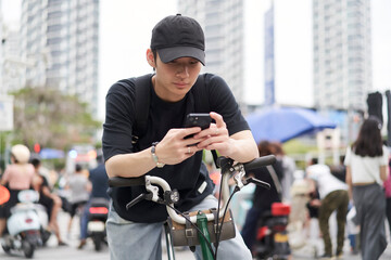 portrait of young Asian man using smartphone when riding bike on street