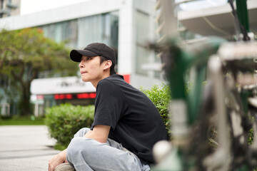 handsome young Asian man sitting on ground beside his bike smiling