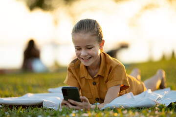 Happy pretty child girl playing video games on her cellphone in summer park