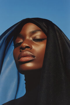 Fashion model posing with elegant black veil and blue fabric against clear sky