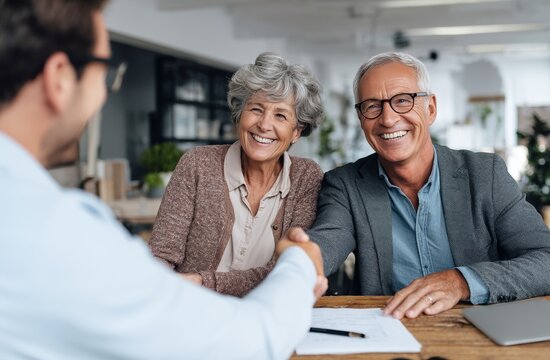 A cheerful elderly couple seals a deal with a consultant via a friendly handshake.