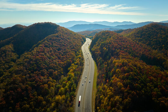 View from above of I-40 freeway in North Carolina heading to Asheville through Appalachian mountains in golden fall season with fast driving trucks and cars. Interstate transportation concept