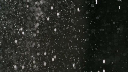 Many bright dust particles of white powder in low light on empty dark black contrast background.