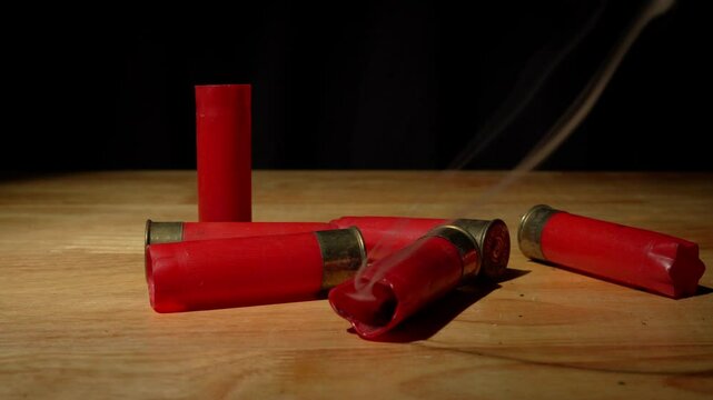 Shotgun shells fall steaming after firing and reloading onto a rough wooden floor