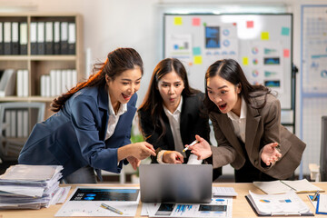 Three women are standing around a laptop, looking at a presentation