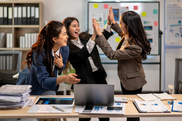Three women are high fiving each other in a business setting