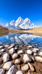 Serene mountain lake reflecting snow-capped peaks under a vibrant blue sky.  Smooth water, rocky shore