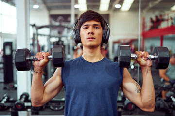 Young athlete lifting dumbbells and listening to music in gym