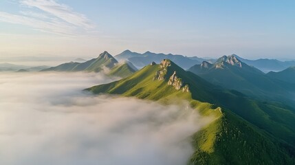 Aerial view of lush green mountain peaks emerging through low clouds at sunrise