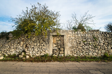 Un muro che delimita una propriet&agrave; agricola con la porta di accesso chiusa con delle pietre, lungo il Cammino del Salento che da Lecce porta a Santa Maria di Leuca