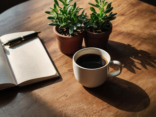 A cozy workspace with black coffee, notebook, and succulents on a wooden table, bathed in warm natural sunlight. Calm and inspiring setup.
