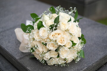 A bouquet of white roses and small flowers is placed on the flat stone with bokeh background