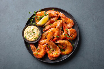 Grilled shrimp with lemon and sauce on a plate. Grey background. Close up. Top view.