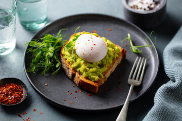 Toast with avocado, poached egg and green salad. Grey background. Close up.