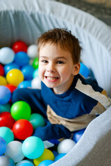 Boy enjoying colorful ball pit playtime. Young boy smiles happily while sitting in a ball pit filled with various colorful plastic balls during playtime.