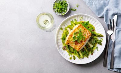 Roasted cod with asparagus and on plate and white wine. Grey background. Copy space. Top view.