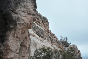 Rocky cliffside landscape with sparse vegetation under overcast sky