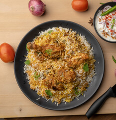 Spicy chicken biryani in pot. served with onion raita	