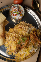 Spicy chicken biryani in pot. served with onion raita	