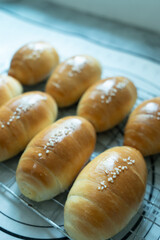 Freshly baked golden bread rolls with sesame seeds, cooling on a wire rack in natural light.
