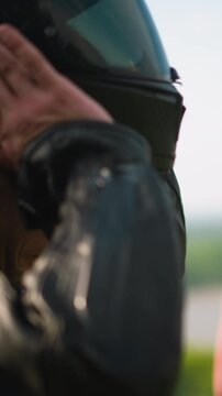 Motorcyclist takes off black helmet and looks at young woman with luxurious long fair hair standing against picturesque lake on spring day closeup slow motion