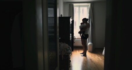 Mother gently cradling baby close while standing near window, sharing intimate and peaceful moment of connection and love in softly lit home environment