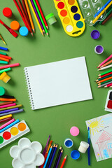 Sketchbook mockup: blank notebook page surrounded by paints and pencils on a green background