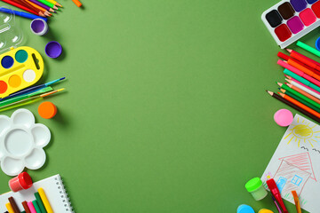 Creative set for children's art: paints, pencils, and an album on a green background, top view