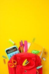 Red school backpack overflowing with stationery on vibrant yellow background. Back to school...