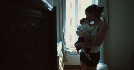 Mother standing by window, cradling baby and gazing down with love and affection, capturing peaceful and intimate family moment at home