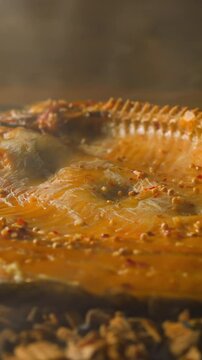 Delicatessen ide fish with spices smoked on wooden shavings and charcoals with rising up steam at bright light in smokehouse closeup slow motion