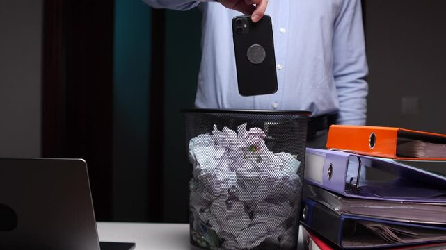 Discarding smartphone into trash bin at office desk