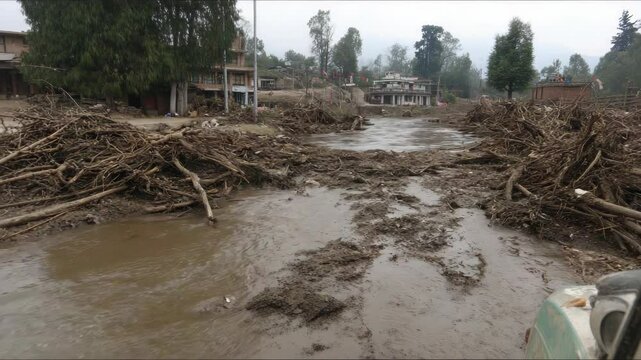 Flood aftermath showing debris and mud covering town near river, houses damaged near water's edge after a natural disaster impacts area.